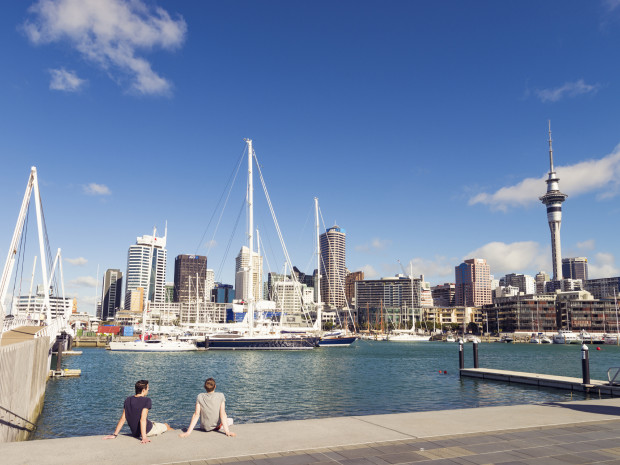 Auckland, New Zealand - February 5, 2013: Two men looking towards Auckland's skyline across the water of the Viaduct Harbour. Two men relaxing by the water of Auckland's Viaduct Harbour.